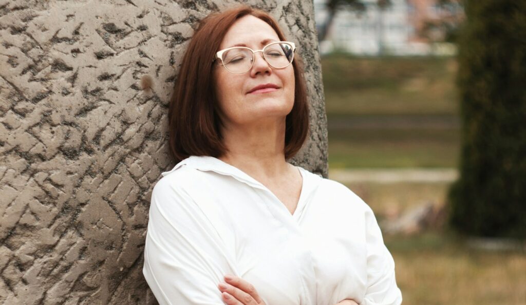 woman in white long sleeve shirt and black skirt standing beside brown tree during daytime