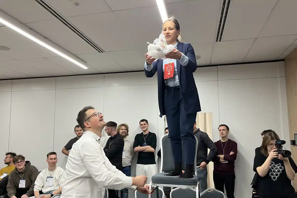 Dr Marta Szewczyk trzyma konstrukcję chroniącą jajko, obok dr Rafał Szewczyk, w tle uczestnicy Cyberiady